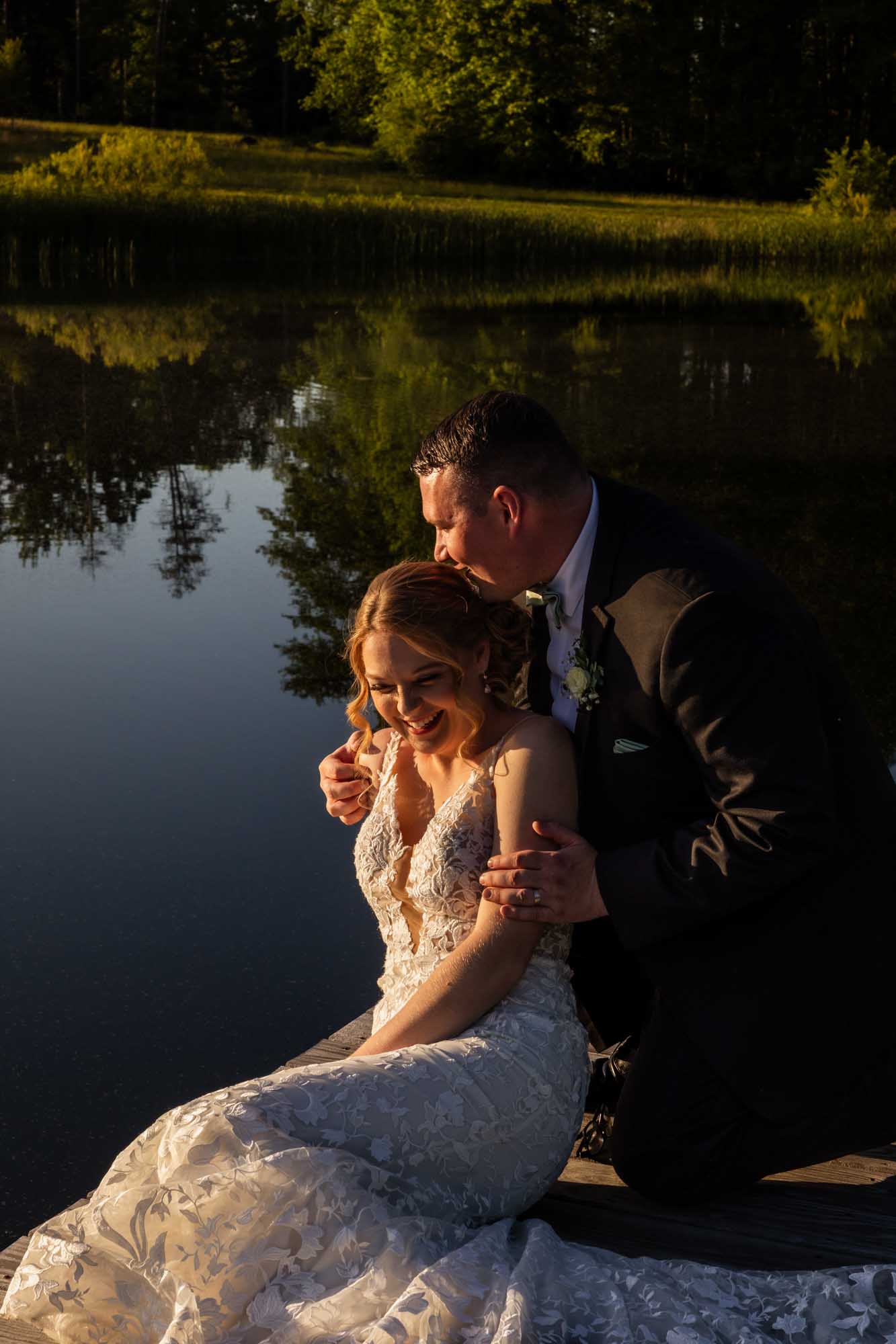 bride and groom laugh together at sunset in front of lake water at pinehall at eisler farm on their wedding day
